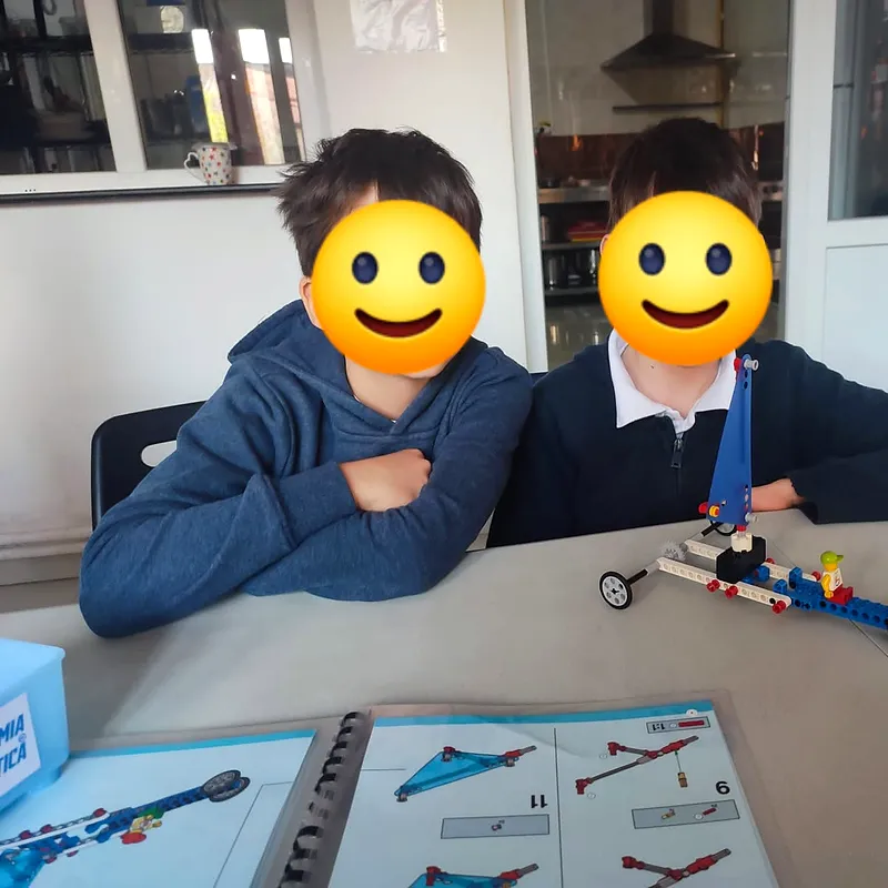 Doi copii lângă o mașinuță construită din LEGO Technic, alături de manualul de instrucțiuni