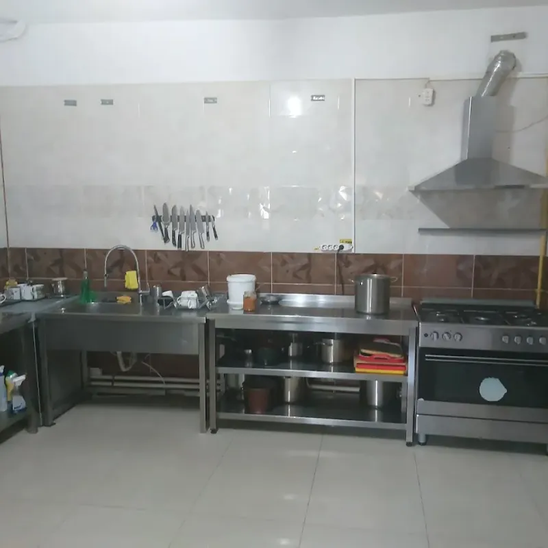 Bucătărie utilată cu blaturi de inox, aragaz profesional și hotă
