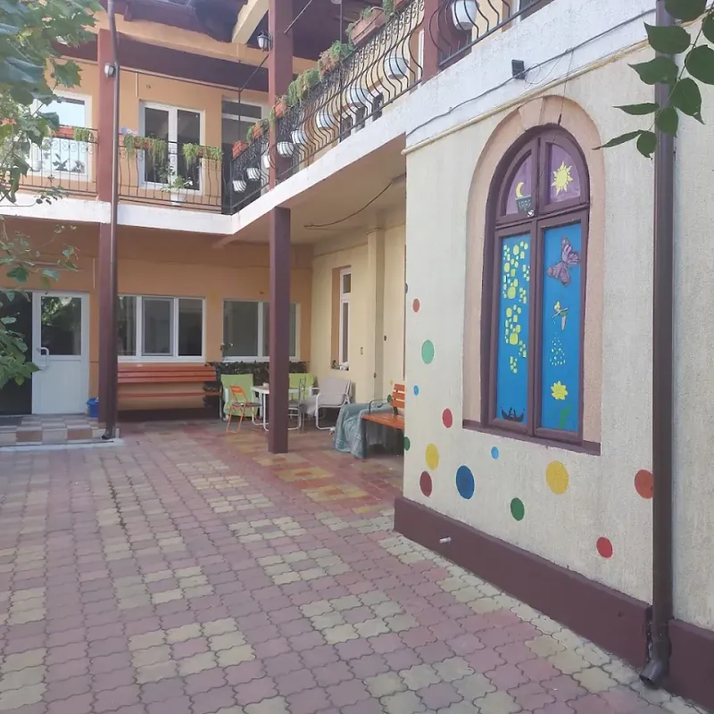 Curtea interioară pavată a After School Bulinela, cu bănci, mese și un perete decorat cu buline colorate
