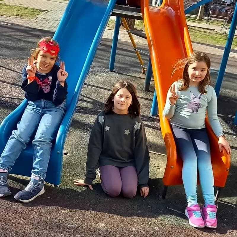 Trei fetițe zâmbind pe toboganul din parcul de lângă after school, într-o zi însorită