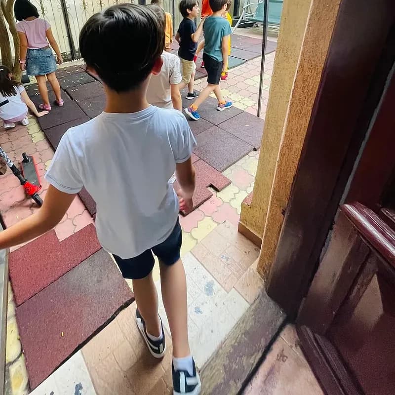 Copii ieșind în curte, sub foișorul verde din curtea after school-ului