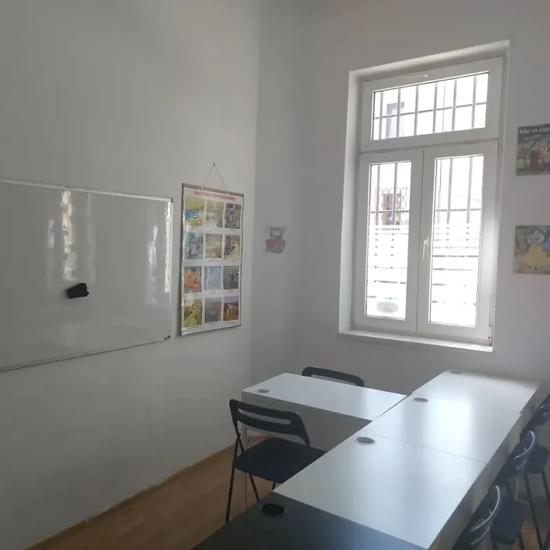Sală de curs cu fereastră mare, tablă albă și planșe în limba engleză pe perete