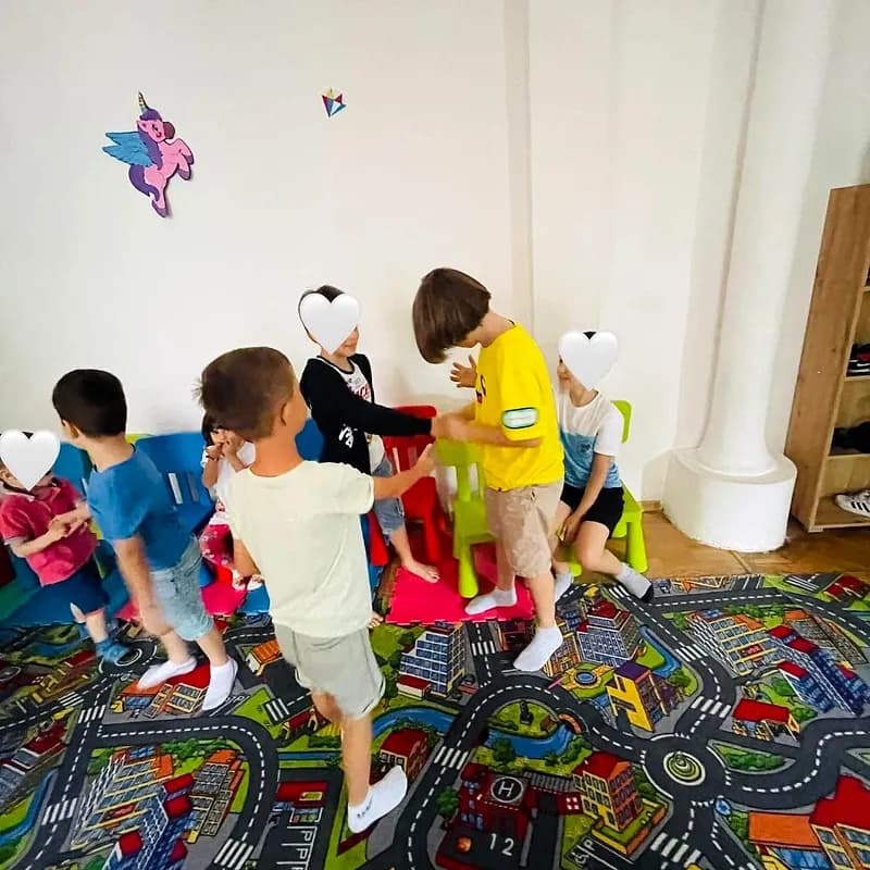 Copii jucând scaunele muzicale în sala de joacă, în jurul unui șir de scăunele colorate